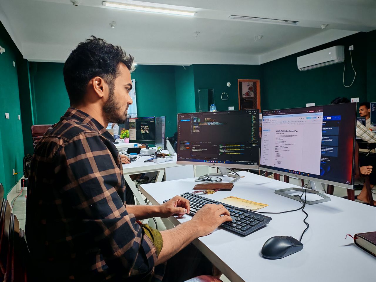 Home A software developer working on code at a dual monitor setup in a modern office.